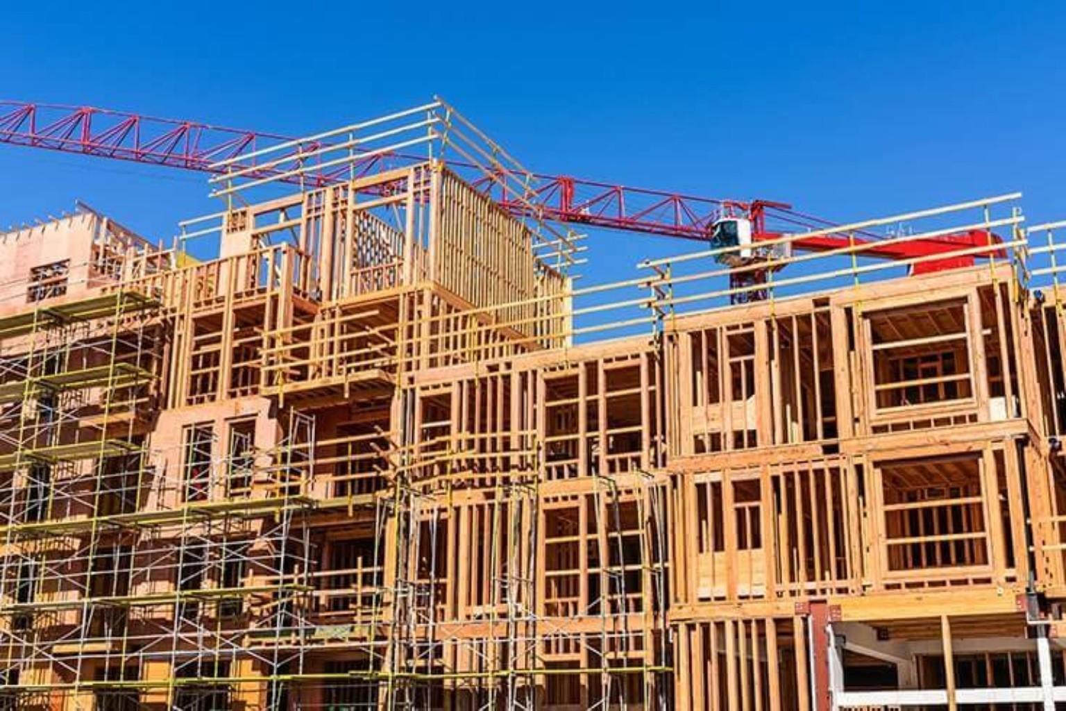 Multifamily apartment construction with exposed timber framing, scaffolding and a red tower crane